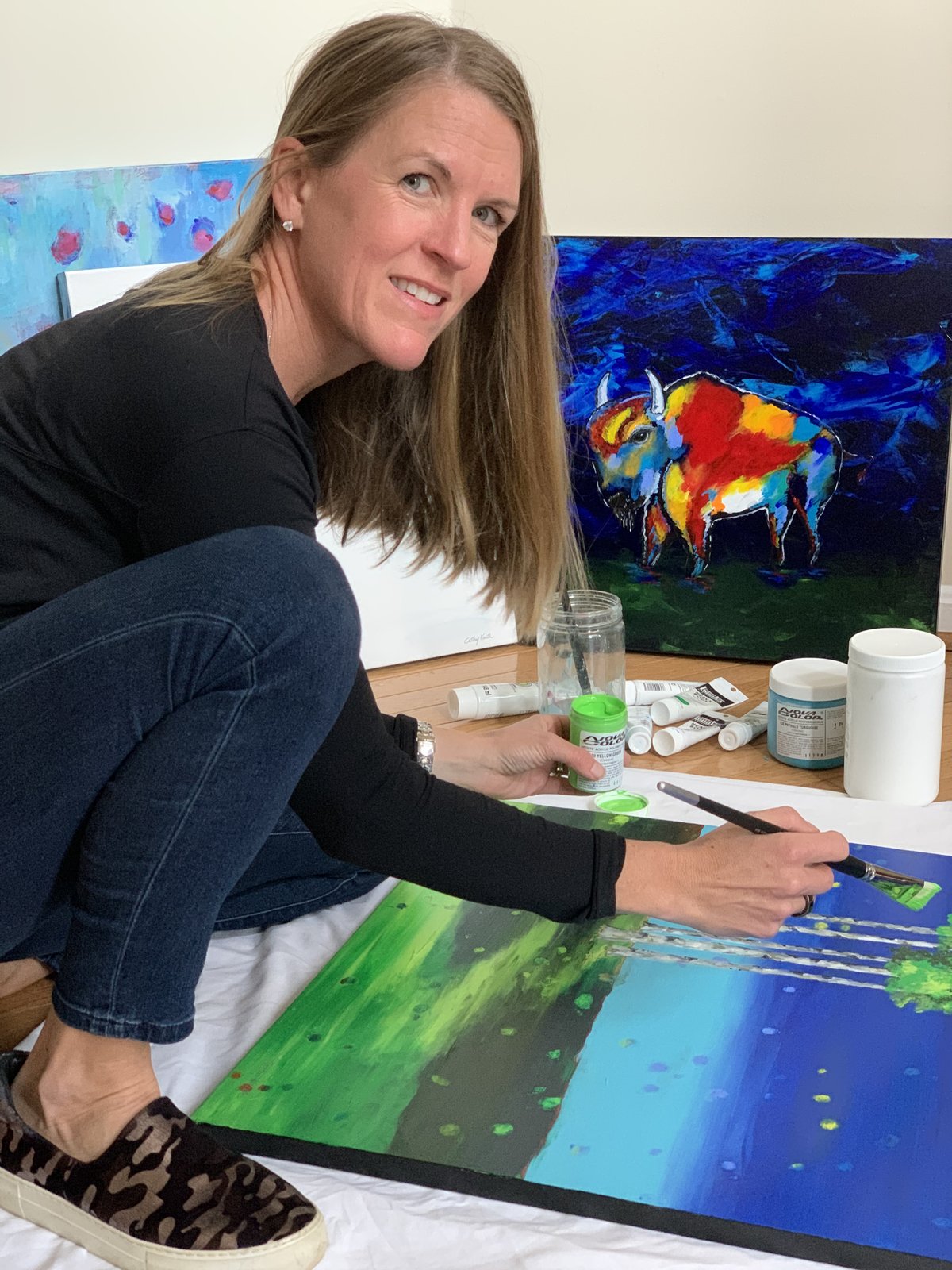 Cathy Keith painting in her studio, finished works behind her